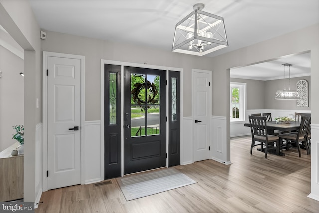 foyer entrance featuring a chandelier, light wood finished floors, a wainscoted wall, and visible vents