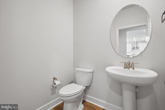 half bath featuring a sink, baseboards, toilet, and wood finished floors
