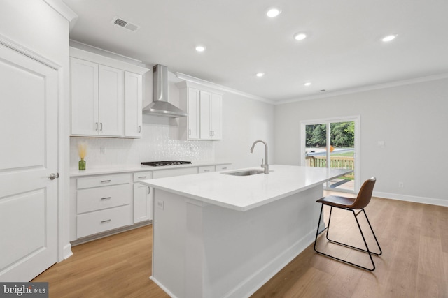 kitchen featuring a sink, light wood-style flooring, wall chimney range hood, and black stovetop