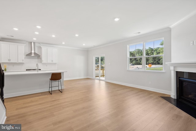 unfurnished living room featuring recessed lighting, a glass covered fireplace, ornamental molding, and light wood-style flooring