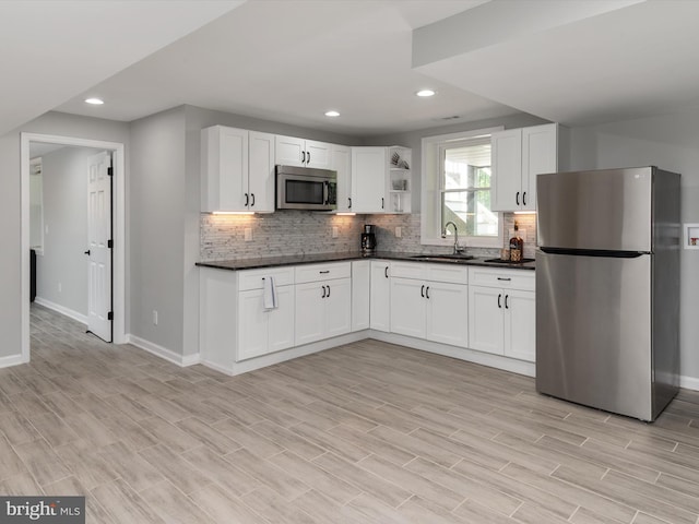 kitchen featuring appliances with stainless steel finishes, baseboards, dark countertops, a sink, and open shelves
