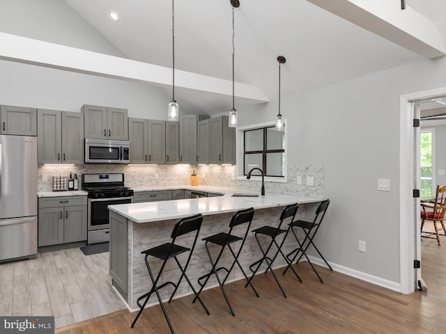 kitchen featuring appliances with stainless steel finishes, gray cabinets, a sink, a peninsula, and a breakfast bar area