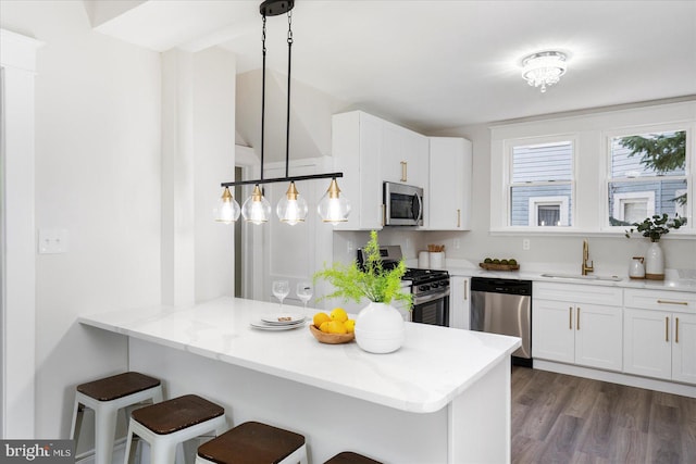 kitchen featuring a peninsula, a breakfast bar, white cabinets, a sink, and appliances with stainless steel finishes
