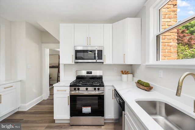 kitchen featuring wood finished floors, white cabinets, light stone counters, a sink, and stainless steel appliances
