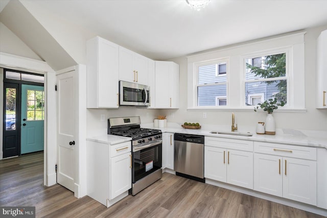 kitchen with light stone countertops, a sink, white cabinets, stainless steel appliances, and light wood-style flooring