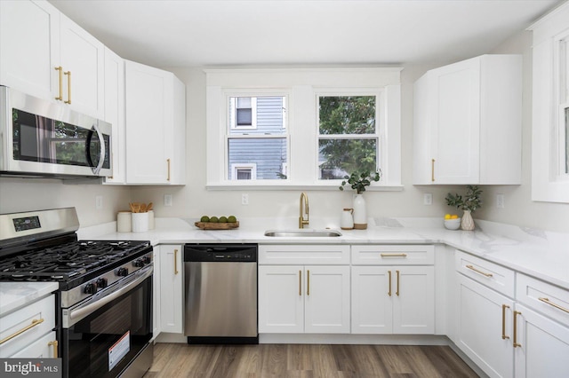 kitchen featuring light stone countertops, appliances with stainless steel finishes, a sink, white cabinetry, and wood finished floors