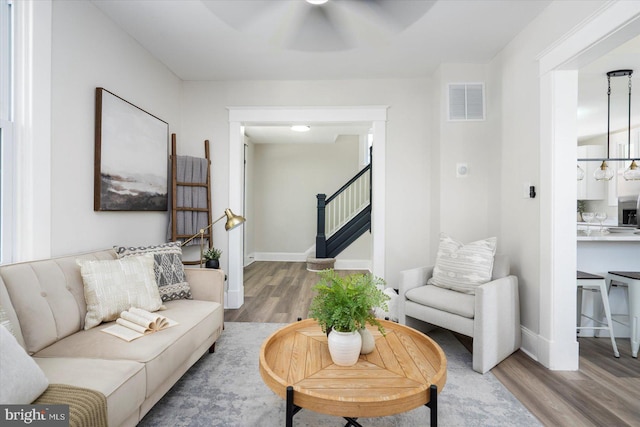 living area featuring a ceiling fan, baseboards, wood finished floors, visible vents, and stairway