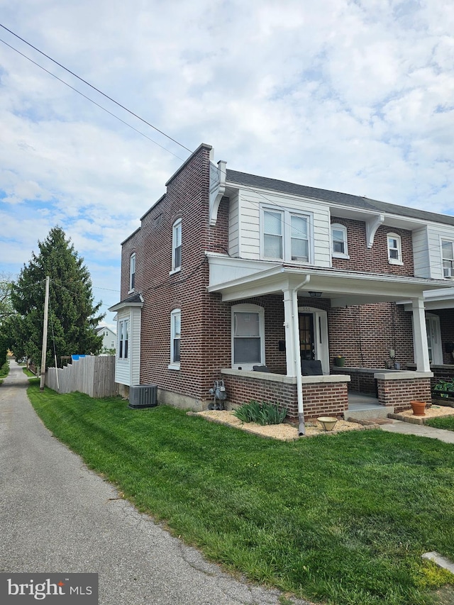 view of front of property with fence, cooling unit, a front lawn, and brick siding