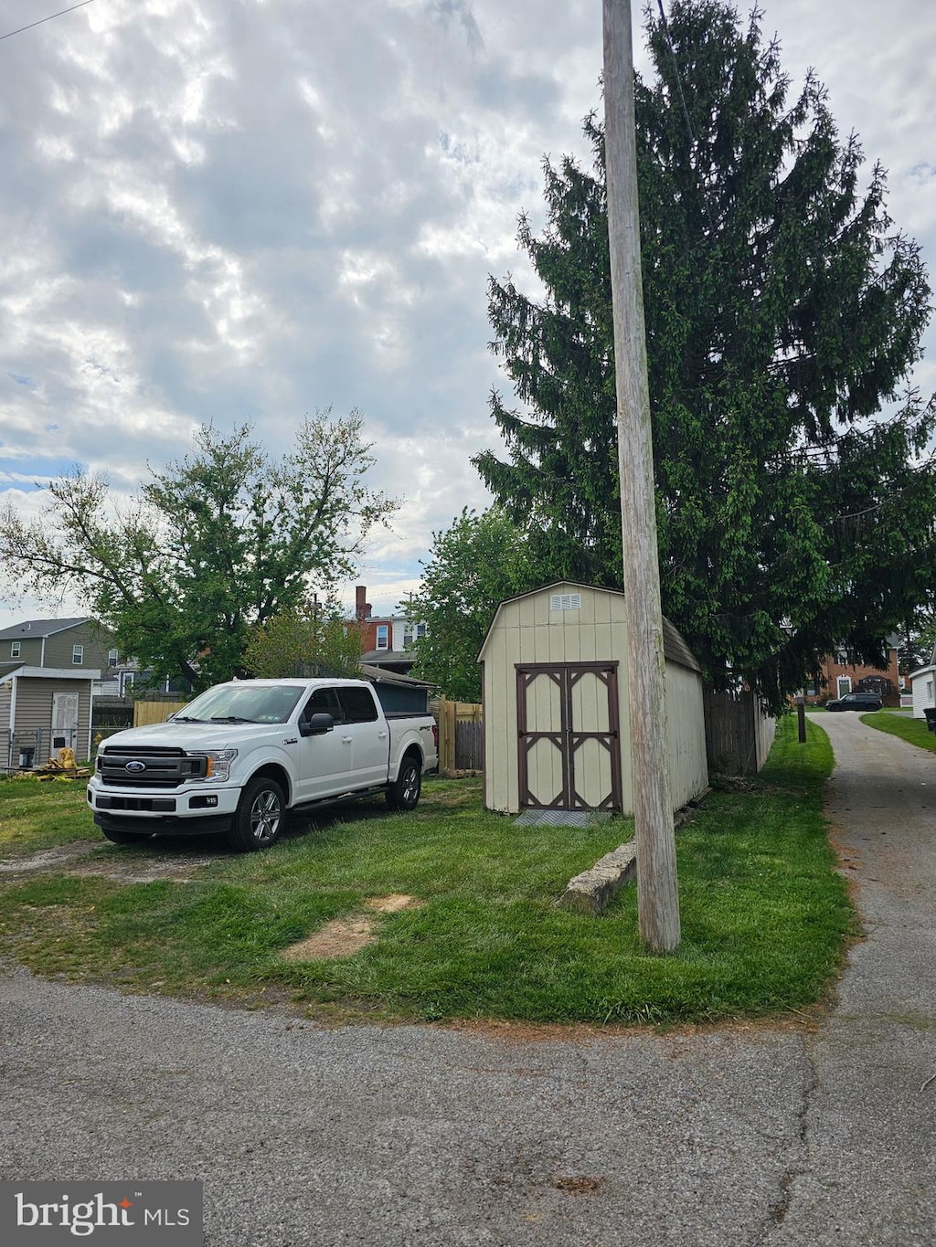 view of vehicle parking with fence and a storage unit