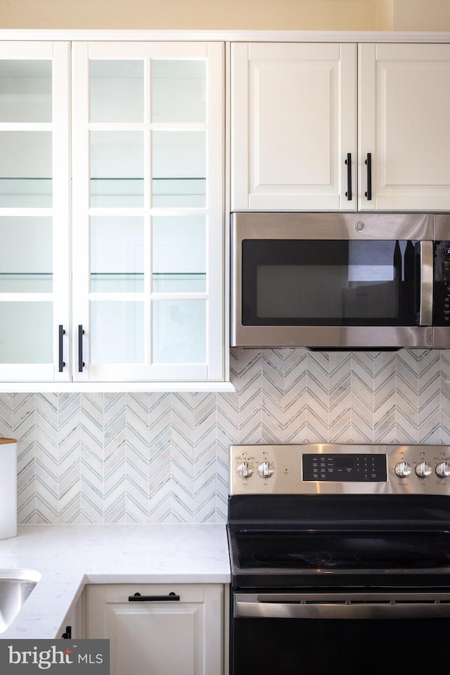 kitchen featuring white cabinets, appliances with stainless steel finishes, decorative backsplash, and light stone counters