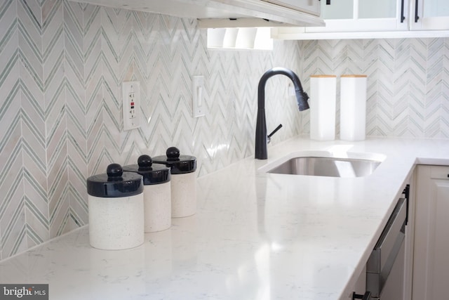 interior details with a sink, white cabinetry, dishwashing machine, and light stone countertops
