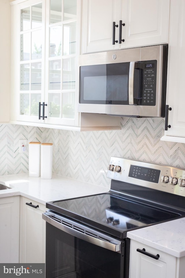 kitchen with white cabinets, stainless steel appliances, light stone countertops, and backsplash