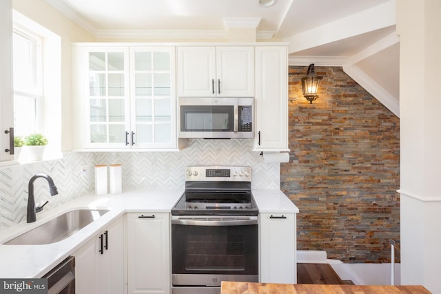 kitchen with appliances with stainless steel finishes, a sink, light countertops, white cabinetry, and backsplash
