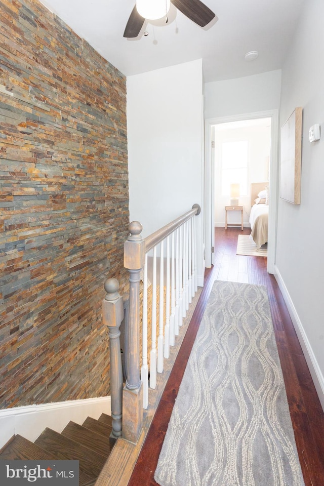 corridor with baseboards, an upstairs landing, and wood finished floors