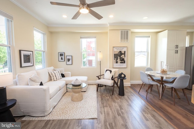 living room featuring ceiling fan, baseboards, wood finished floors, visible vents, and ornamental molding