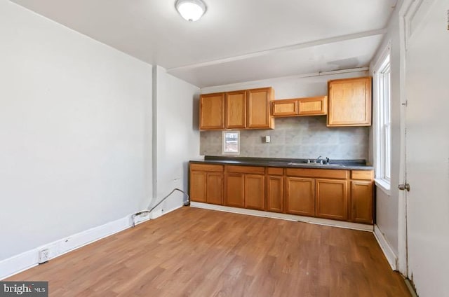 kitchen with decorative backsplash, brown cabinetry, a sink, baseboards, and light wood-style floors
