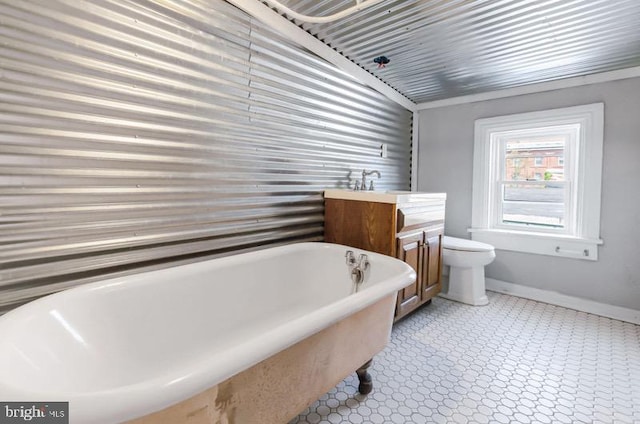 bathroom featuring vanity, toilet, tile patterned floors, baseboards, and a freestanding tub