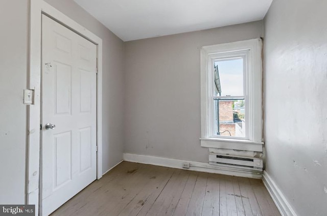 empty room with baseboards, a baseboard radiator, and hardwood / wood-style floors