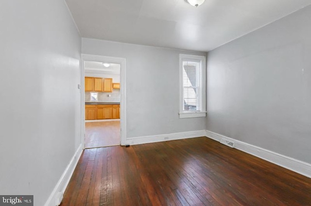 spare room featuring baseboards, dark wood-style flooring, and visible vents