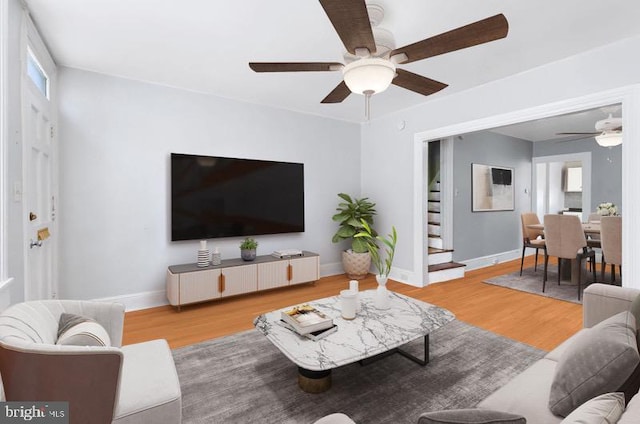 living room with stairs, a ceiling fan, baseboards, and wood finished floors