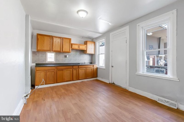 kitchen with visible vents, tasteful backsplash, a sink, baseboards, and light wood-style floors