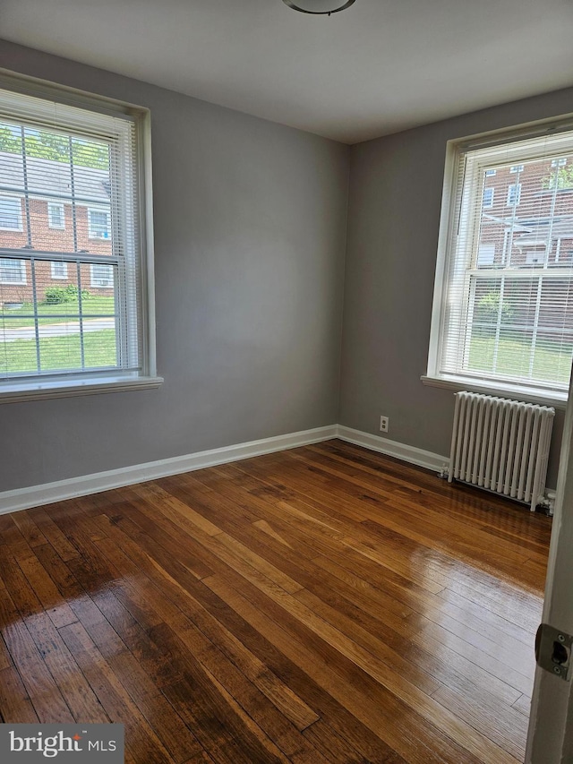 spare room featuring radiator, plenty of natural light, baseboards, and dark wood-style flooring