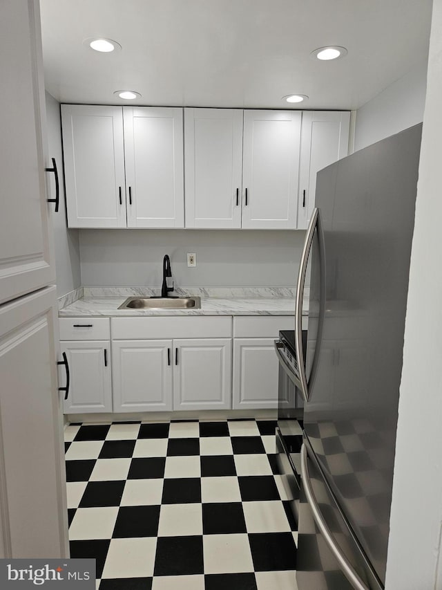 kitchen with freestanding refrigerator, a sink, white cabinetry, and light countertops