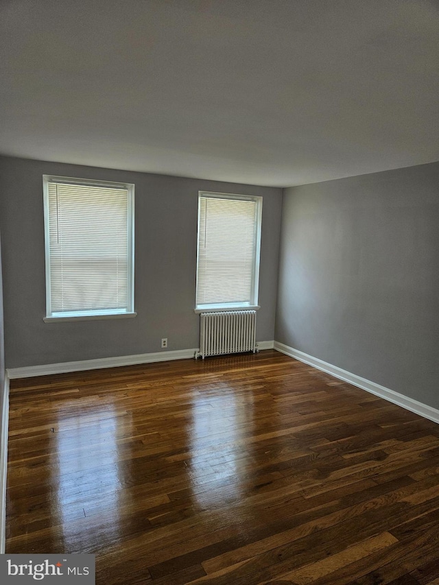 empty room featuring radiator heating unit, baseboards, and dark wood-style flooring