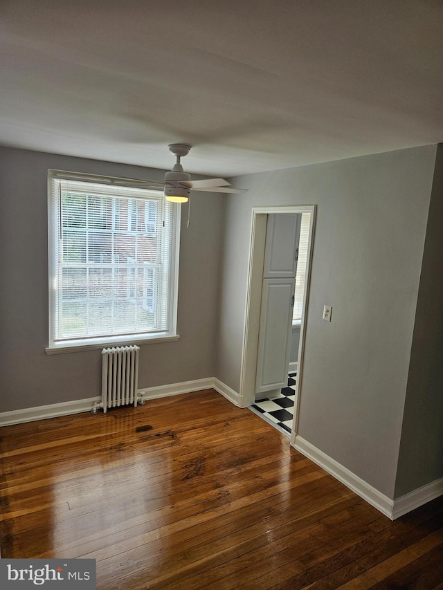 empty room with radiator heating unit, baseboards, wood-type flooring, and a ceiling fan