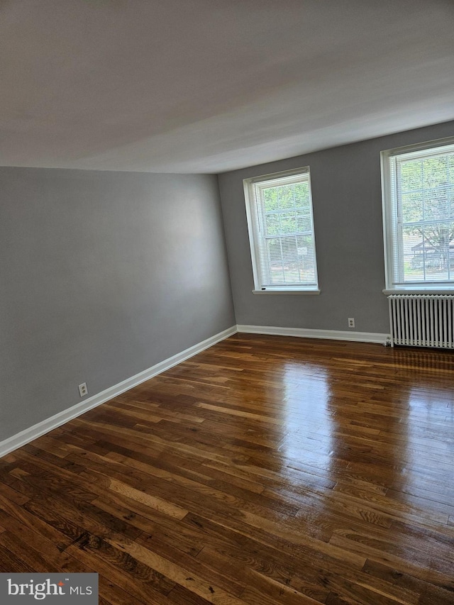 unfurnished room featuring baseboards, dark wood finished floors, and radiator