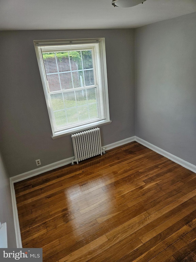 unfurnished room featuring baseboards, radiator, and wood finished floors