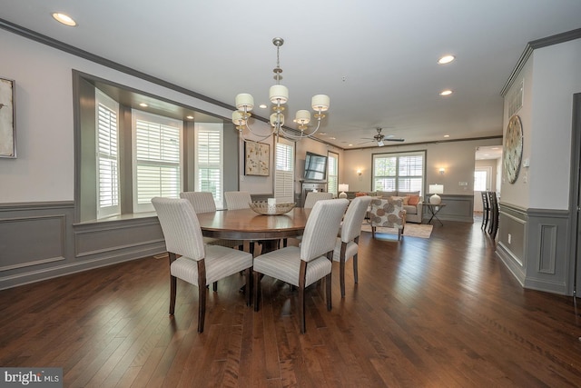 dining area with crown molding, a wainscoted wall, ceiling fan with notable chandelier, and dark wood-style flooring