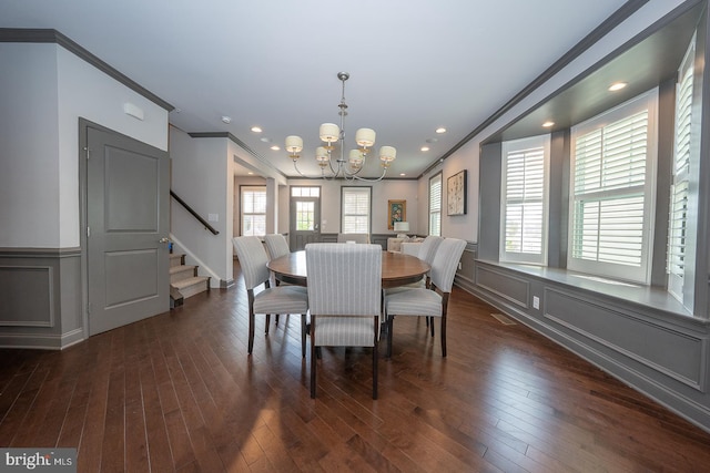 dining area featuring crown molding, a decorative wall, a chandelier, dark wood finished floors, and stairs