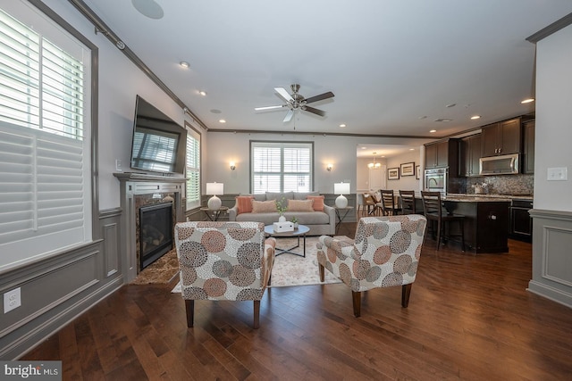 living room featuring a ceiling fan, a fireplace, wainscoting, recessed lighting, and dark wood-type flooring