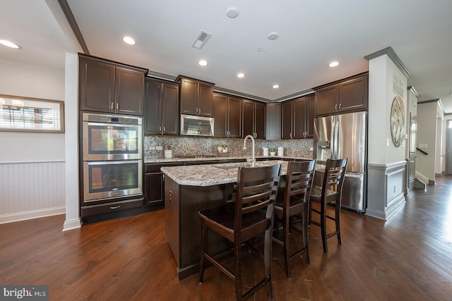 kitchen with decorative backsplash, dark brown cabinets, a sink, dark wood finished floors, and stainless steel appliances