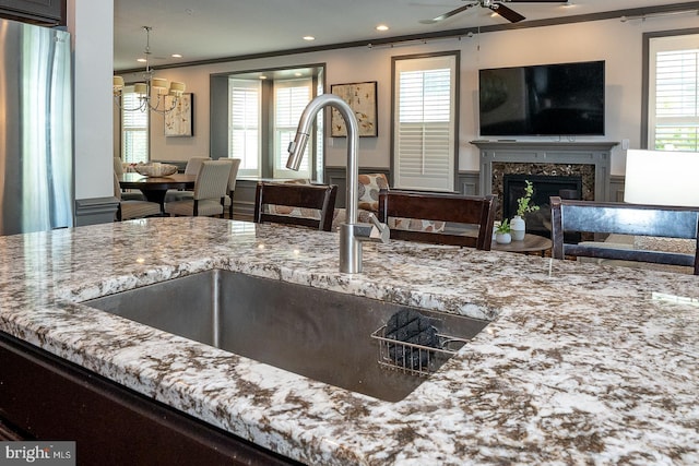 kitchen featuring light stone countertops, open floor plan, a sink, ceiling fan with notable chandelier, and a premium fireplace