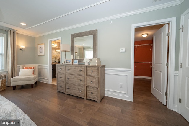 bedroom with crown molding, a walk in closet, a wainscoted wall, and dark wood-style floors
