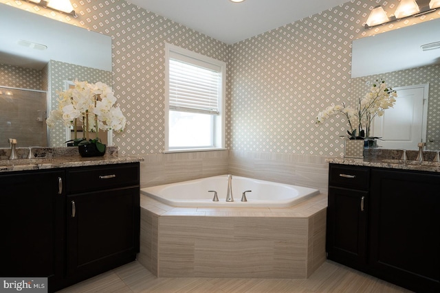 bathroom featuring a sink, a bath, two vanities, and wallpapered walls
