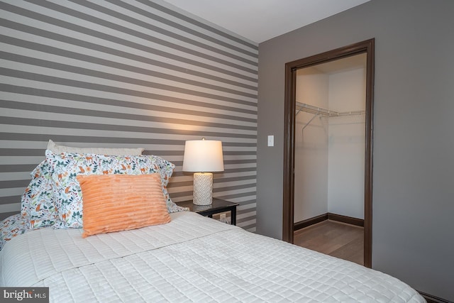 bedroom featuring a closet, an accent wall, wood finished floors, wallpapered walls, and a spacious closet