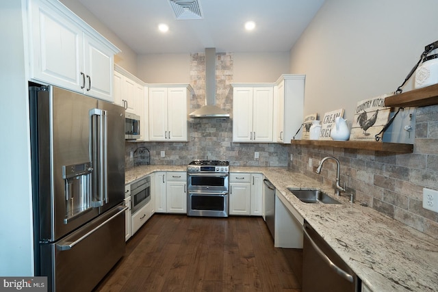 kitchen featuring wall chimney range hood, light stone countertops, appliances with stainless steel finishes, a sink, and visible vents