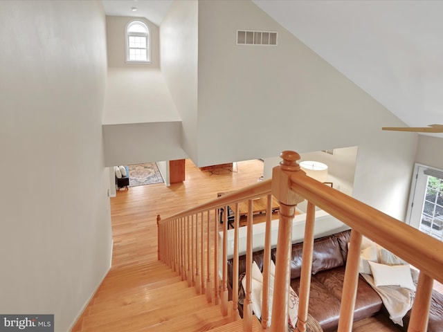 stairs with visible vents, wood finished floors, a healthy amount of sunlight, and high vaulted ceiling