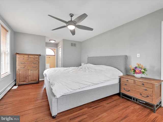 bedroom with ceiling fan, visible vents, baseboard heating, connected bathroom, and light wood-style floors