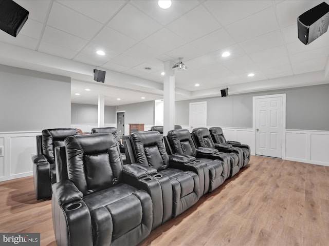 home theater featuring light wood-style floors, wainscoting, and a decorative wall