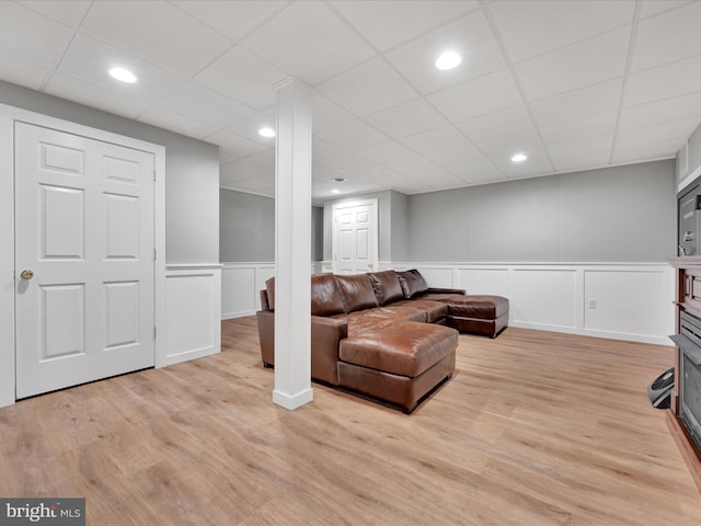 living area featuring a paneled ceiling, wainscoting, light wood-style floors, a decorative wall, and recessed lighting