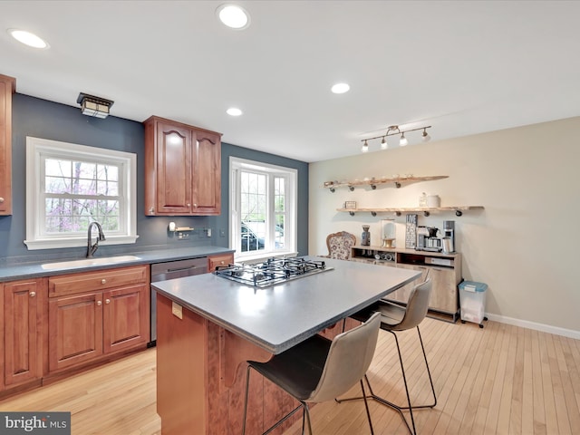 kitchen featuring a breakfast bar area, appliances with stainless steel finishes, a center island, a sink, and light wood-style flooring