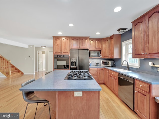 kitchen with a center island, a sink, light wood finished floors, a breakfast bar, and stainless steel appliances