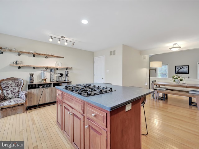 kitchen featuring visible vents, a kitchen island, a breakfast bar, light wood-style floors, and black gas stovetop