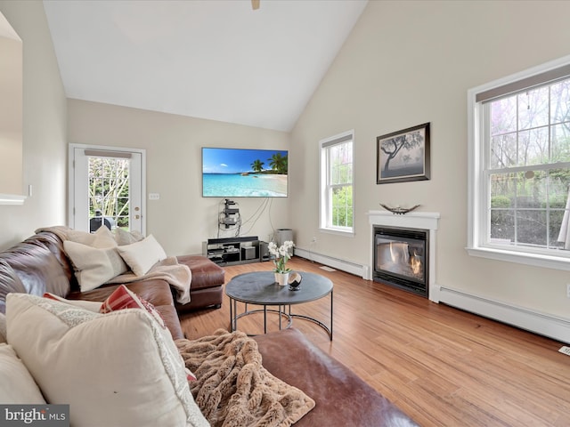 living room featuring a glass covered fireplace, high vaulted ceiling, baseboard heating, and wood finished floors