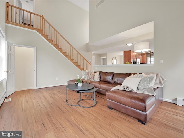 living room featuring visible vents, a towering ceiling, wood finished floors, baseboards, and stairway