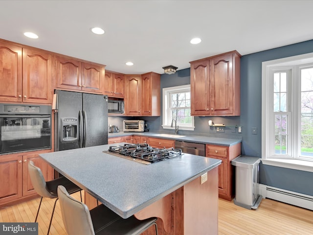 kitchen with a sink, light wood finished floors, a baseboard radiator, and black appliances